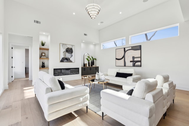 living room with a high ceiling, an inviting chandelier, and light hardwood / wood-style floors