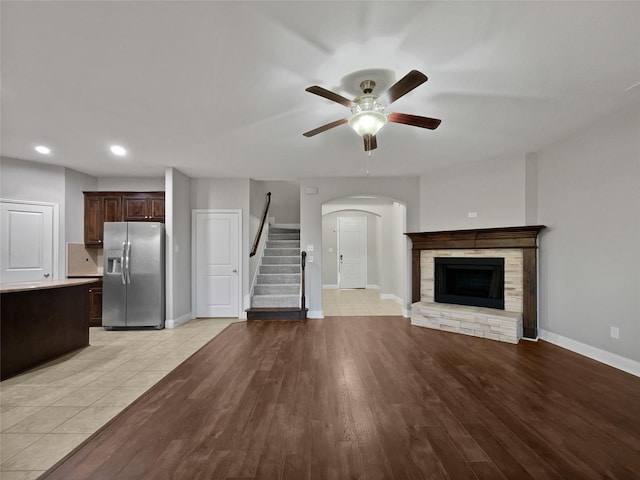 unfurnished living room featuring a stone fireplace, light hardwood / wood-style flooring, and ceiling fan