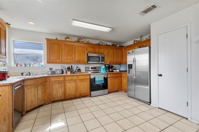 kitchen with sink, light tile patterned flooring, a textured ceiling, and appliances with stainless steel finishes