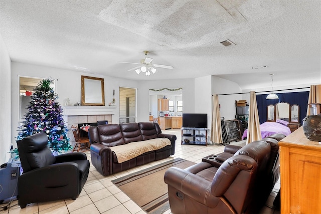 tiled living room with ceiling fan, a tile fireplace, and a textured ceiling