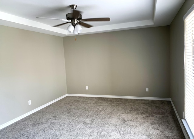 spare room with ceiling fan, a tray ceiling, and carpet