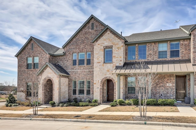 townhome / multi-family property with a standing seam roof, stone siding, a shingled roof, metal roof, and brick siding