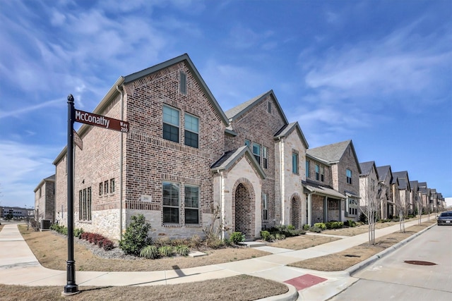 view of front facade featuring brick siding, stone siding, central AC unit, and a residential view