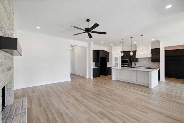 kitchen featuring an island with sink, ceiling fan, a fireplace, light hardwood / wood-style floors, and decorative backsplash