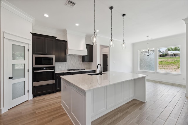 kitchen featuring built in microwave, sink, a center island with sink, custom range hood, and oven