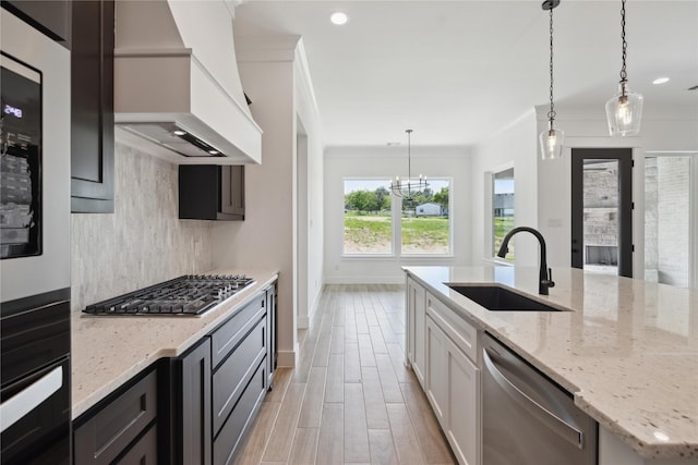 kitchen with sink, stainless steel appliances, light stone countertops, decorative light fixtures, and custom exhaust hood