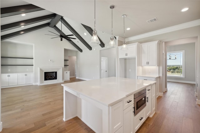 kitchen featuring a kitchen island, stainless steel microwave, decorative light fixtures, white cabinetry, and ceiling fan