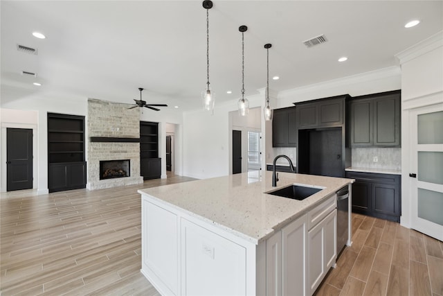 kitchen featuring sink, dishwasher, a kitchen island with sink, light stone countertops, and a stone fireplace