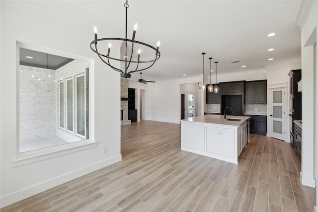 kitchen featuring sink, decorative light fixtures, an island with sink, a fireplace, and decorative backsplash