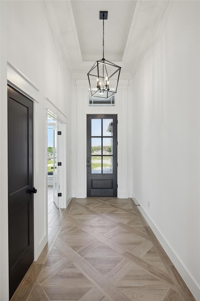 doorway to outside with a raised ceiling, light parquet flooring, and a notable chandelier