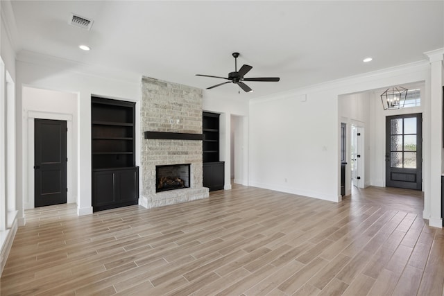 unfurnished living room featuring ceiling fan with notable chandelier, a fireplace, light hardwood / wood-style flooring, crown molding, and built in shelves