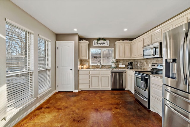 kitchen with sink, stainless steel appliances, light stone countertops, decorative backsplash, and cream cabinetry