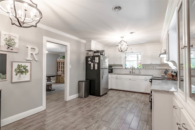 kitchen featuring sink, stainless steel refrigerator, an inviting chandelier, hanging light fixtures, and white cabinets