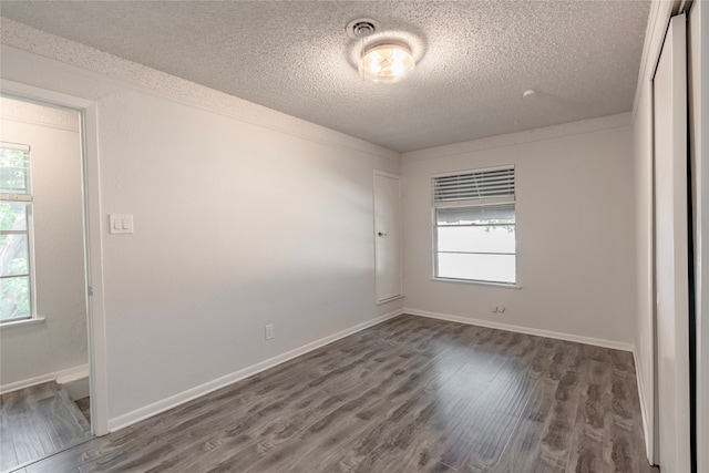 empty room with a healthy amount of sunlight, dark hardwood / wood-style floors, and a textured ceiling