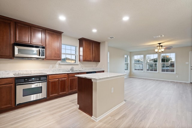 kitchen with appliances with stainless steel finishes, sink, a center island, light stone counters, and light hardwood / wood-style flooring