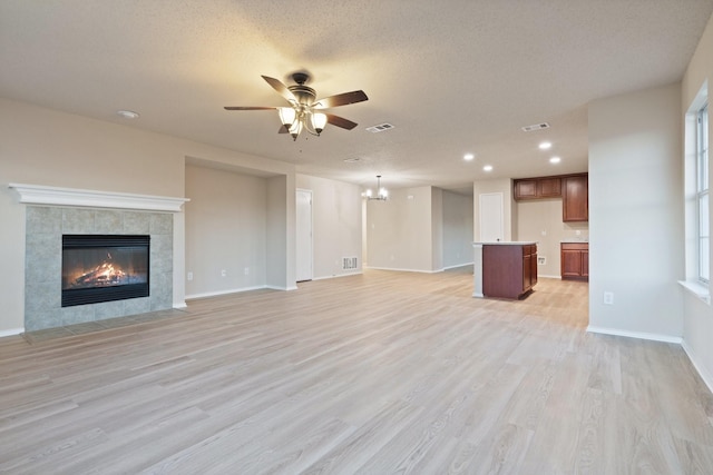 unfurnished living room featuring ceiling fan, a fireplace, light hardwood / wood-style flooring, and a textured ceiling