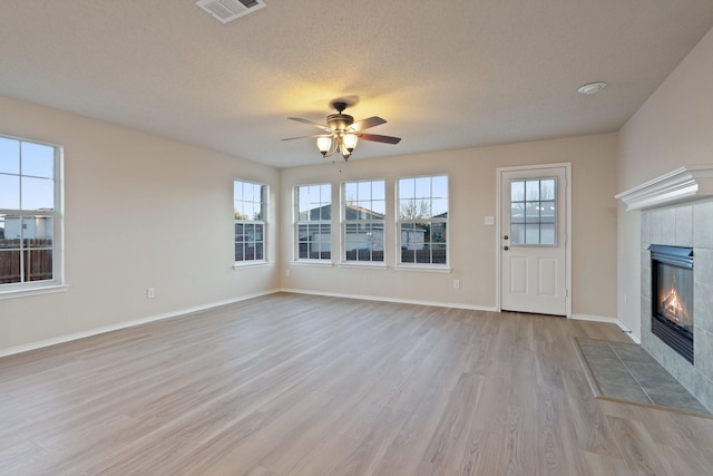 unfurnished living room with ceiling fan, light hardwood / wood-style flooring, a tile fireplace, and a textured ceiling