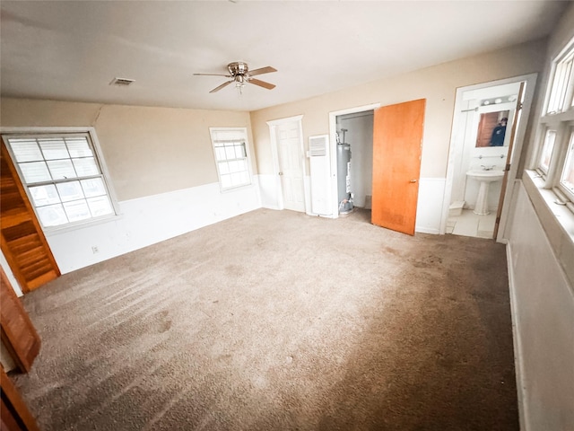 unfurnished bedroom with sink, ensuite bath, ceiling fan, carpet flooring, and gas water heater