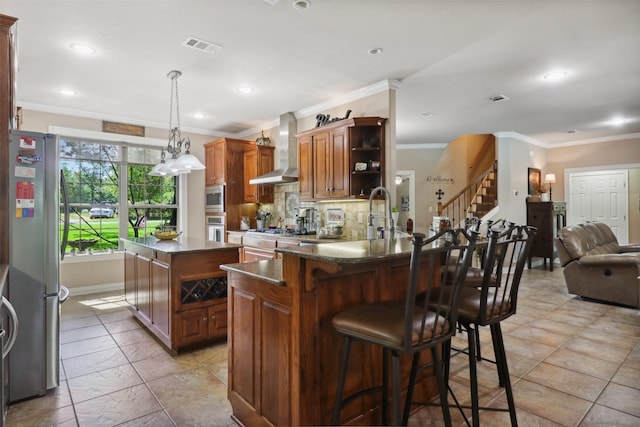 kitchen featuring a center island, appliances with stainless steel finishes, a kitchen breakfast bar, decorative backsplash, and wall chimney range hood