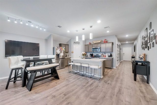 kitchen with appliances with stainless steel finishes, pendant lighting, an island with sink, a kitchen bar, and light hardwood / wood-style flooring