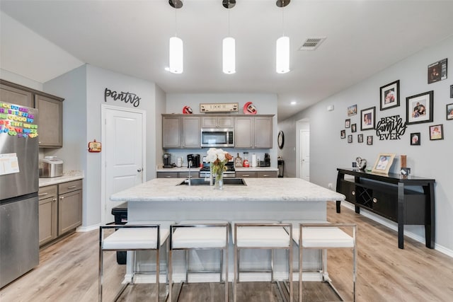 kitchen featuring hanging light fixtures, stainless steel appliances, an island with sink, and light wood-type flooring