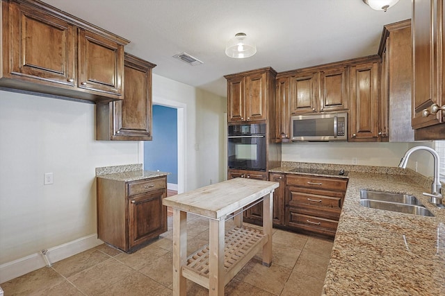 kitchen with light tile patterned flooring, light stone countertops, sink, and black oven