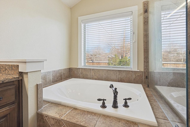 bathroom with a relaxing tiled tub, vanity, and a healthy amount of sunlight