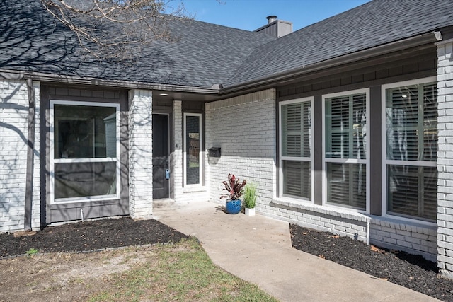 property entrance with roof with shingles, a chimney, and brick siding