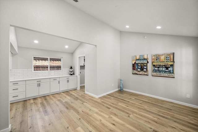 interior space with light wood finished floors, baseboards, vaulted ceiling, and decorative backsplash