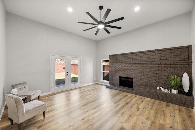 living area with french doors, a brick fireplace, a ceiling fan, and light wood-style floors