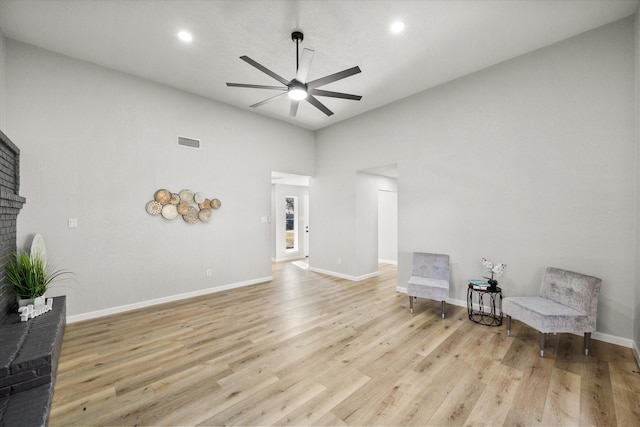 sitting room with ceiling fan, visible vents, baseboards, light wood-type flooring, and a brick fireplace