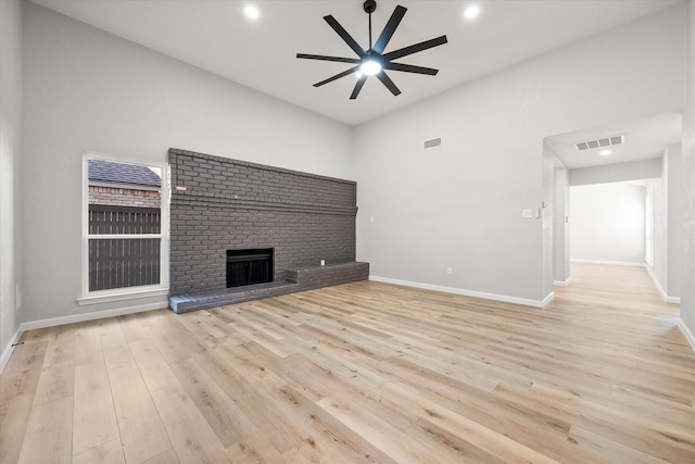 unfurnished living room featuring ceiling fan, light hardwood / wood-style floors, a brick fireplace, and a high ceiling