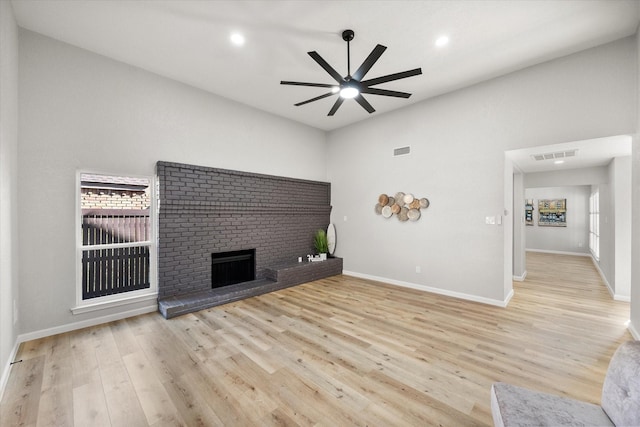 unfurnished living room with visible vents, a ceiling fan, a brick fireplace, light wood-type flooring, and baseboards