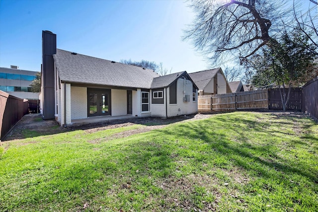 rear view of house featuring a chimney, brick siding, a lawn, and a fenced backyard