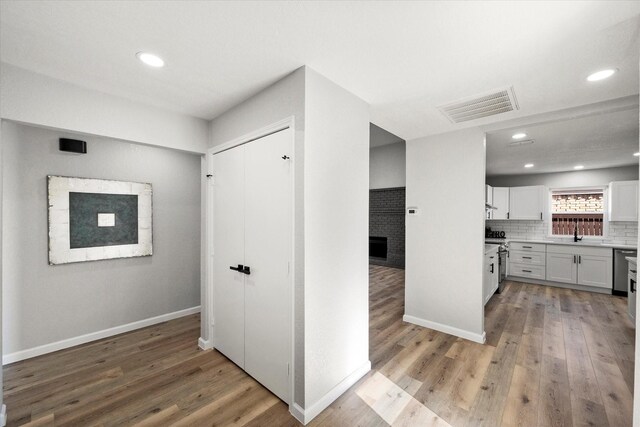 kitchen with sink, white cabinetry, light wood-type flooring, a fireplace, and decorative backsplash