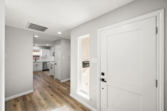 hallway with baseboards, visible vents, light wood-type flooring, a sink, and recessed lighting