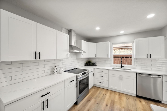 kitchen with stainless steel appliances, white cabinetry, a sink, and wall chimney exhaust hood