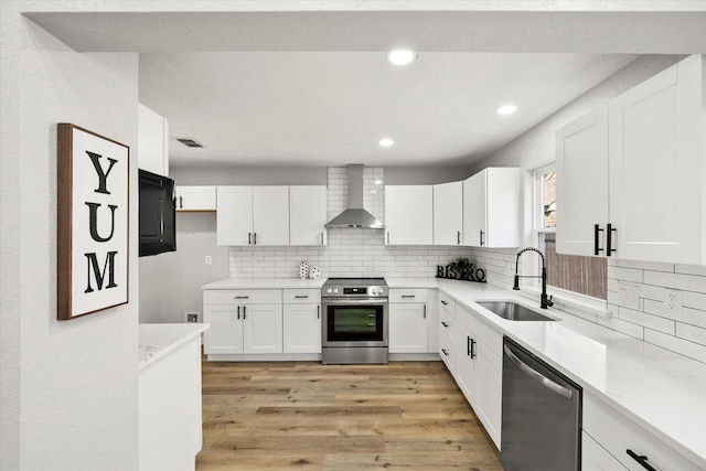 kitchen with a sink, white cabinetry, light countertops, appliances with stainless steel finishes, and wall chimney range hood