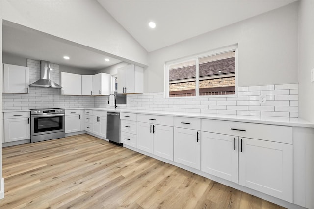 kitchen with lofted ceiling, wall chimney range hood, sink, appliances with stainless steel finishes, and white cabinets