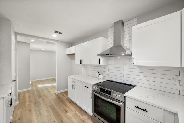 kitchen featuring wall chimney range hood, light stone countertops, white cabinetry, and stainless steel range with electric cooktop