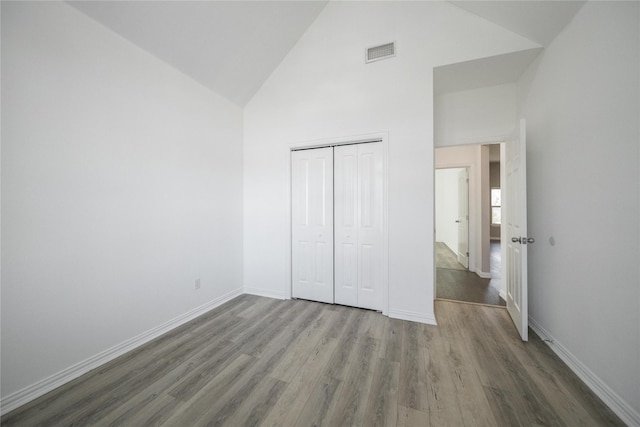 unfurnished bedroom featuring hardwood / wood-style flooring, high vaulted ceiling, and a closet