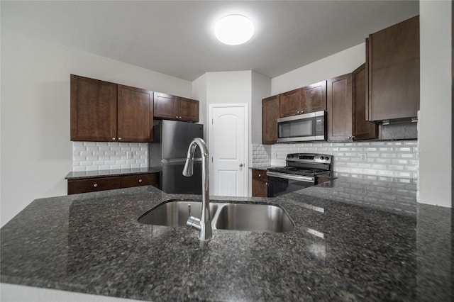 kitchen with appliances with stainless steel finishes, sink, decorative backsplash, dark stone counters, and dark brown cabinetry