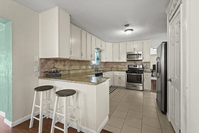 kitchen featuring tasteful backsplash, stainless steel appliances, kitchen peninsula, and stone countertops