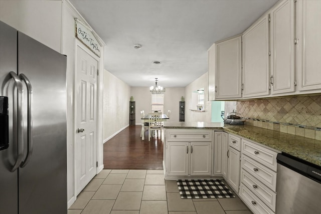 kitchen with appliances with stainless steel finishes, kitchen peninsula, dark stone counters, and white cabinets