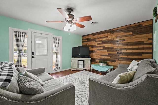 living room with hardwood / wood-style floors, wooden walls, and ceiling fan