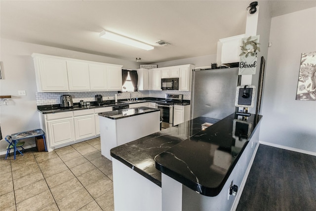 kitchen with light tile patterned floors, white cabinetry, backsplash, electric range, and a kitchen island