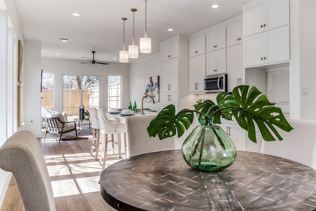 kitchen with pendant lighting, white cabinetry, sink, ceiling fan, and light hardwood / wood-style flooring