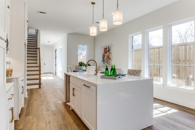 kitchen featuring sink, light hardwood / wood-style flooring, white cabinetry, a kitchen island with sink, and decorative light fixtures