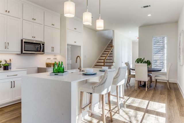 kitchen featuring decorative light fixtures, an island with sink, and white cabinets