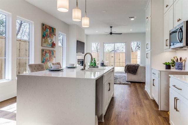 kitchen featuring pendant lighting, white cabinetry, sink, and a center island with sink